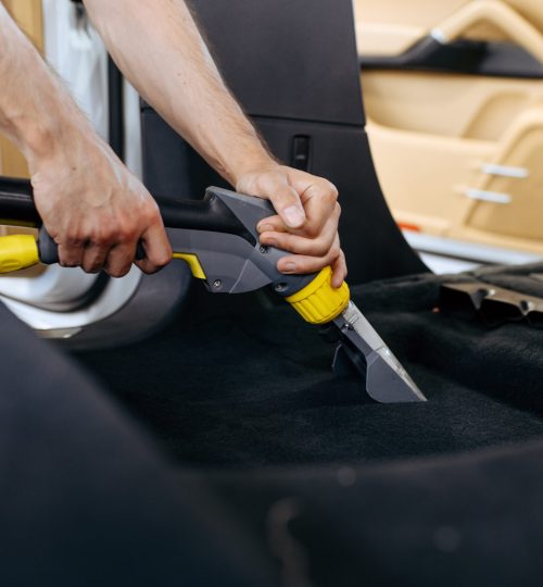 Worker cleans car interior with vacuum cleaner